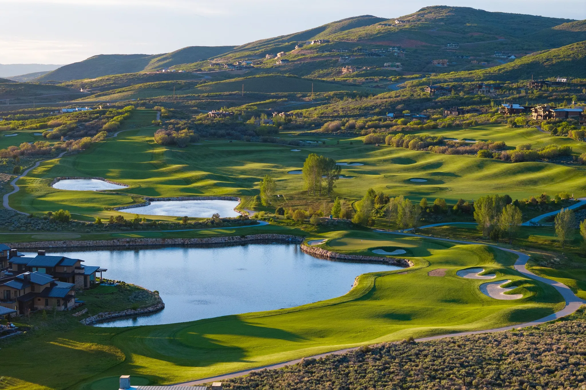 Expansive golf course setting featuring manicured greens, multiple water features, sand traps, and golf cart paths