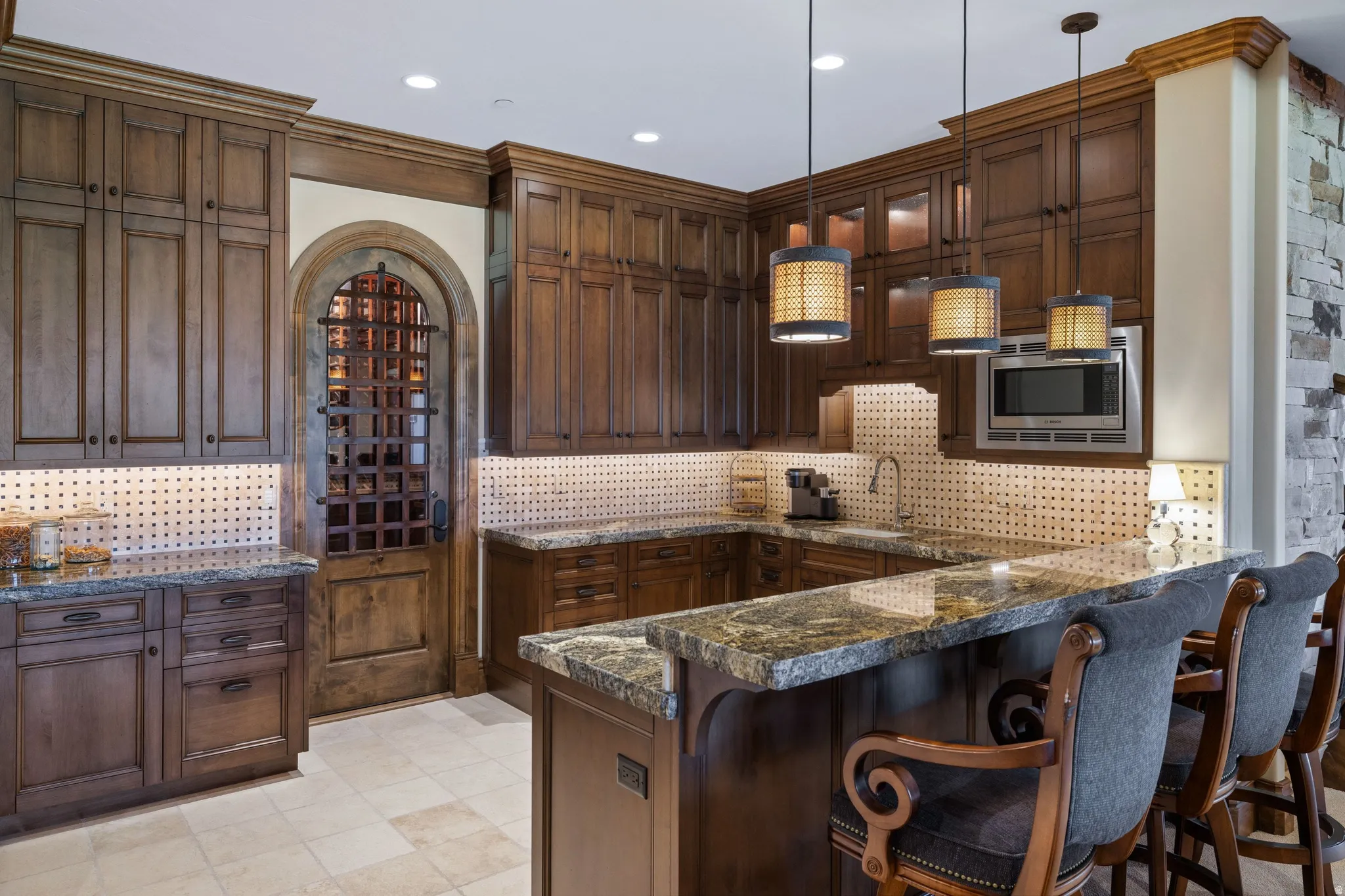Gourmet kitchen with rich wood cabinetry, stone countertops, integrated microwave, custom wine cellar door, and tile flooring