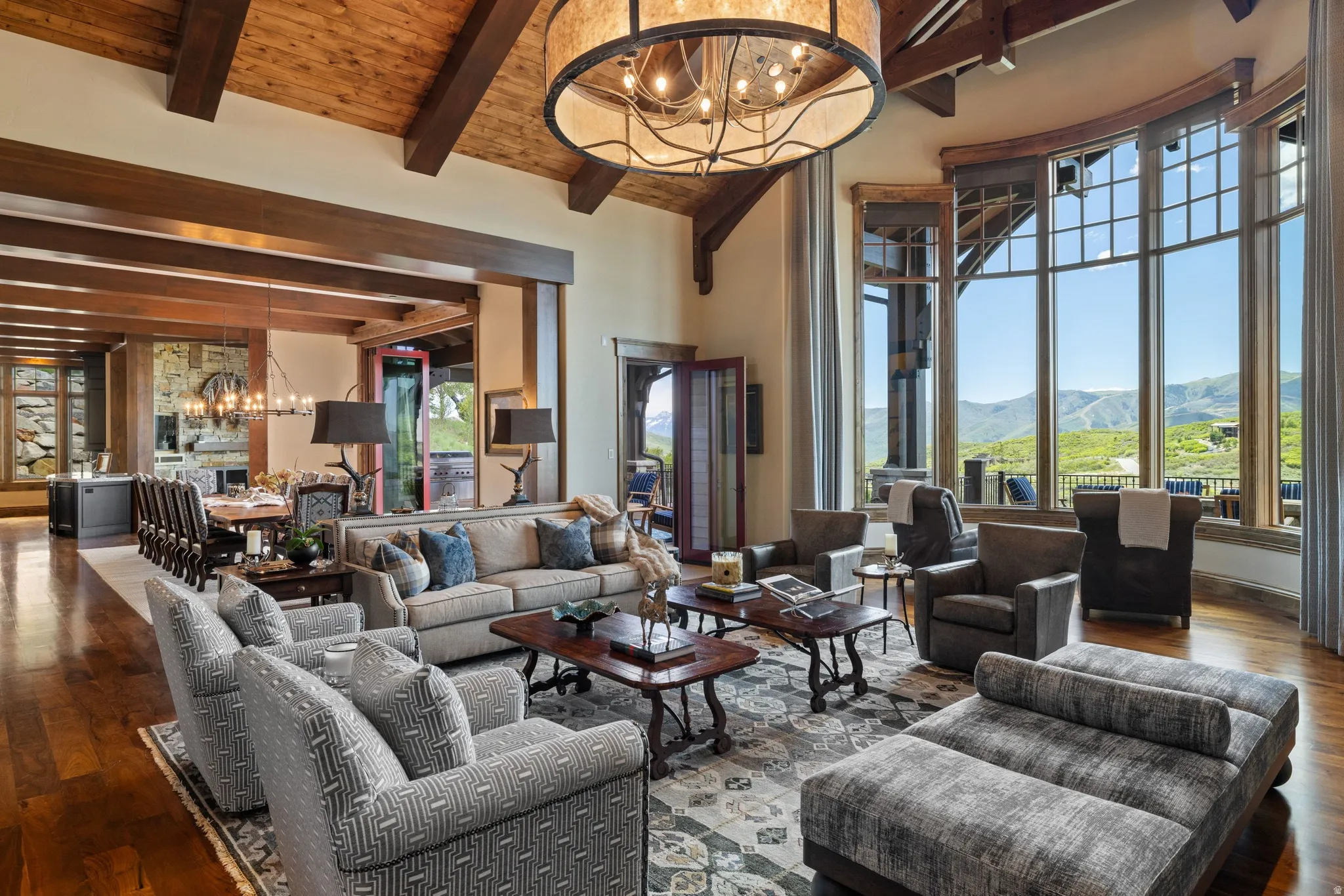 Grand living room with wood-finish flooring, exposed beam ceiling, and a large circular chandelier