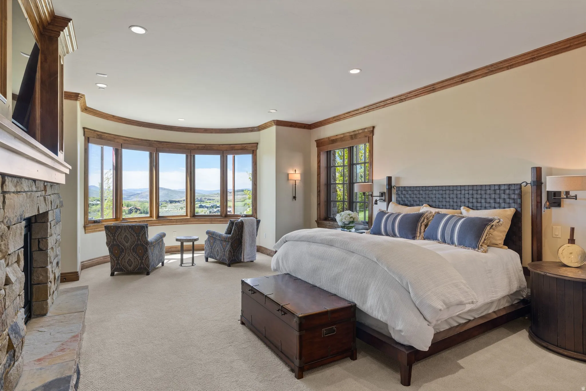 Spacious room featuring a stone-clad fireplace, a curved bay window with wood-frame windows, recessed lighting, and crown molding