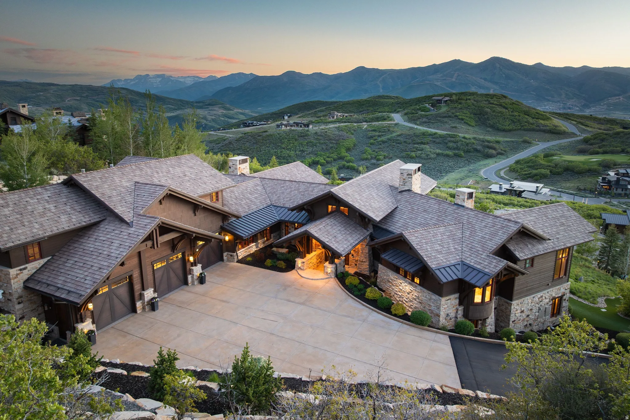 Expansive property featuring a stone and wood facade, multiple gabled roofs, an attached multi-car garage, a paved driveway, and mature landscaping, all set against a mountainous backdrop