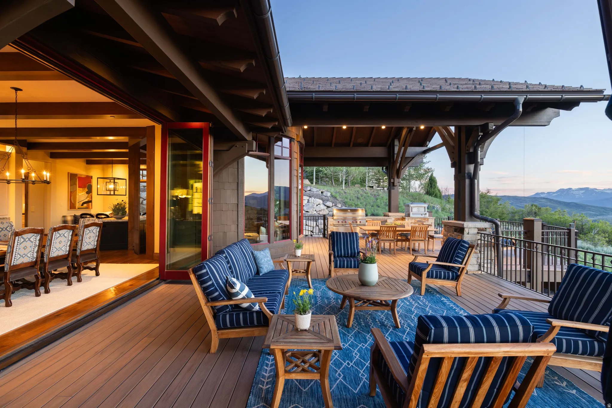 Expansive outdoor deck featuring wood-finish decking, a covered patio area with exposed timber beams, a built-in outdoor kitchen, and a metal railing system