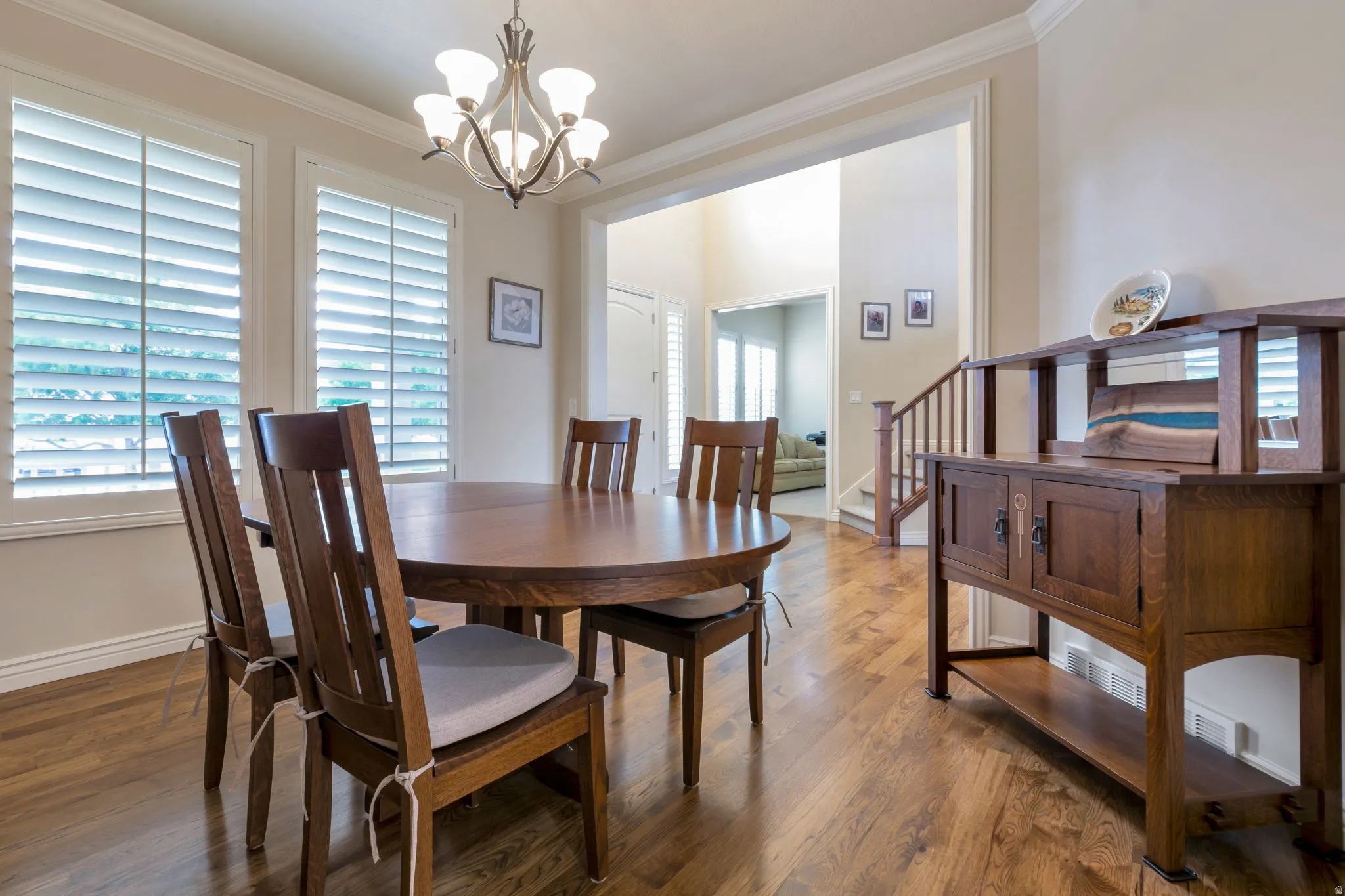 Hardwood-finish flooring throughout, featuring a traditional chandelier, crown molding, and plantation shutters