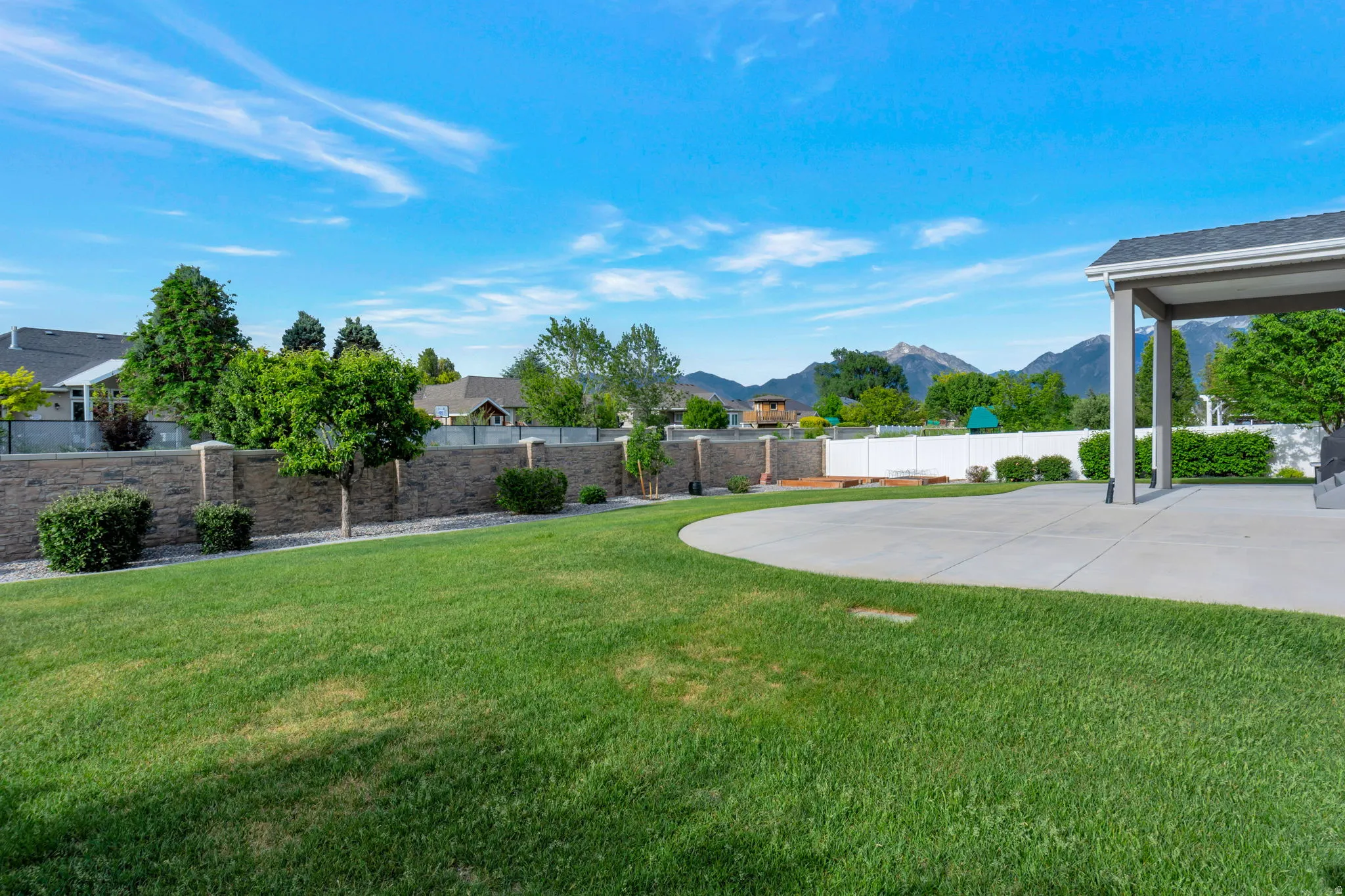 Expansive backyard featuring a manicured lawn, a large concrete patio, and a covered patio area with a gray roof