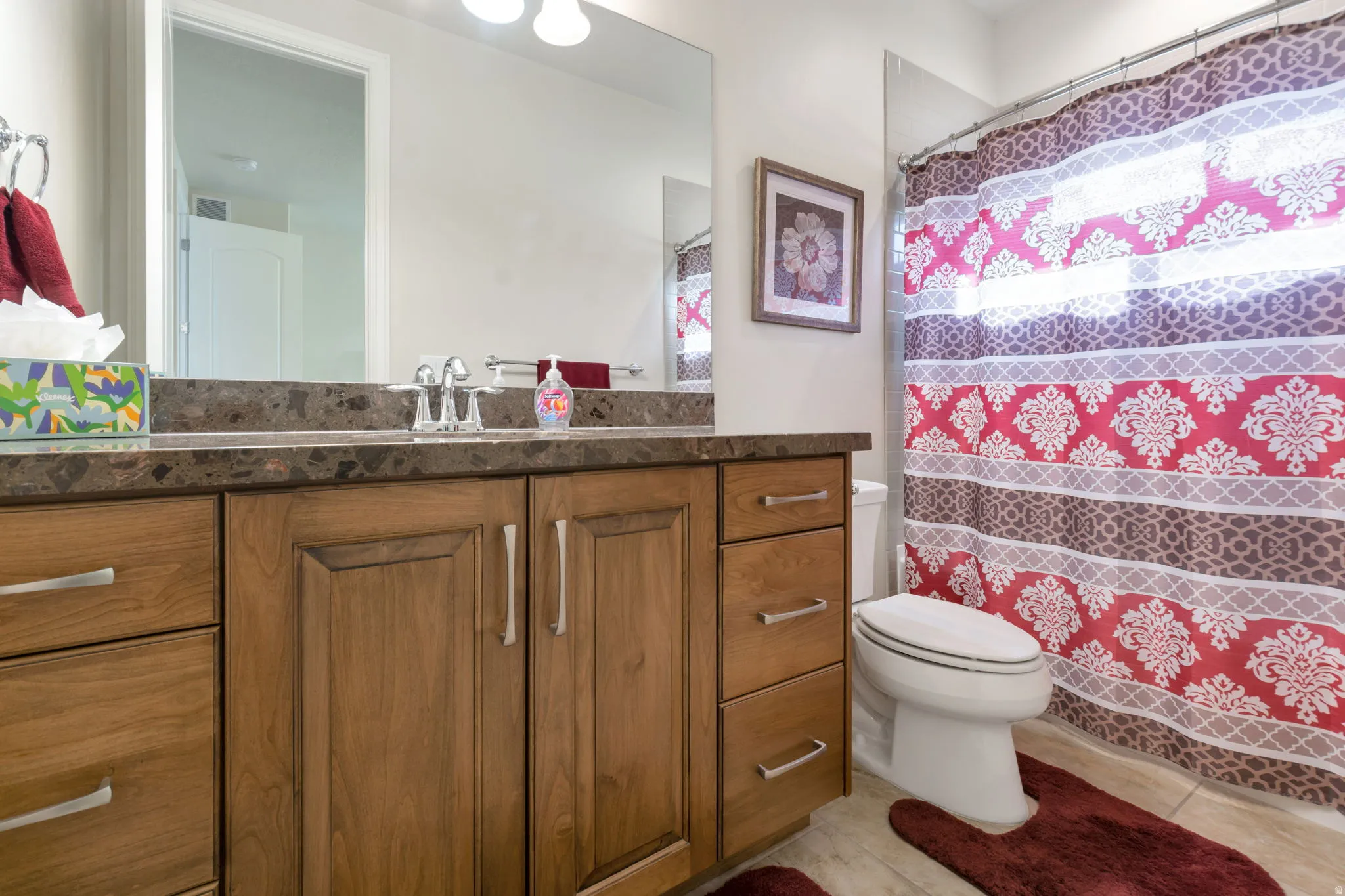 Bathroom featuring a long wood-finish vanity with a stone-look countertop, a single basin sink with a chrome faucet, and a large wall-mounted mirror