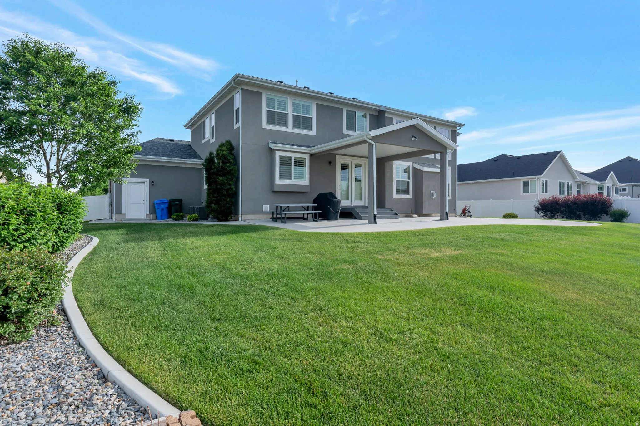Expansive green lawn with a defined concrete border, leading to a large concrete patio with a covered section