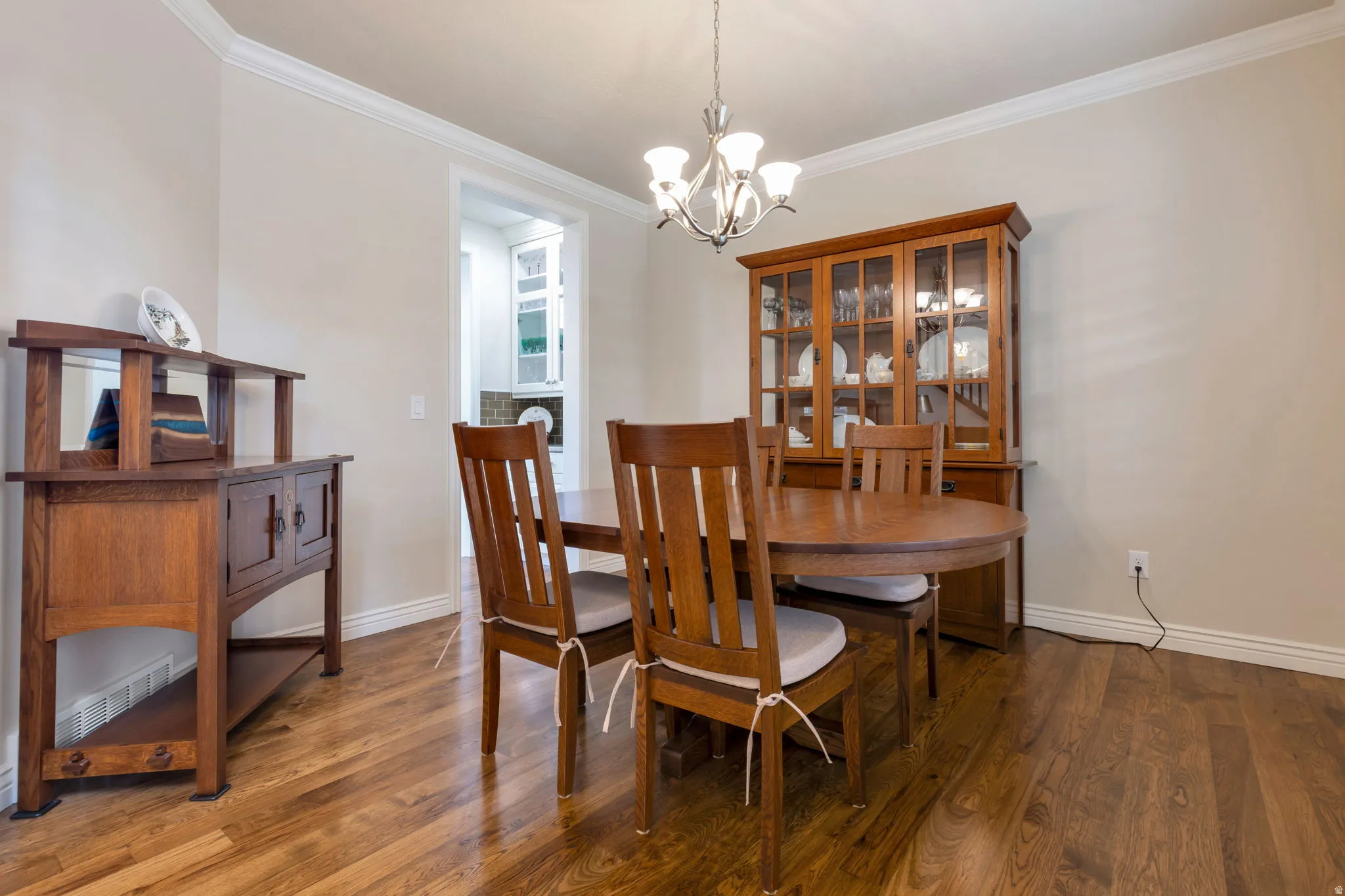 Wood-finish flooring throughout, featuring crown molding, baseboards, and a contemporary chandelier