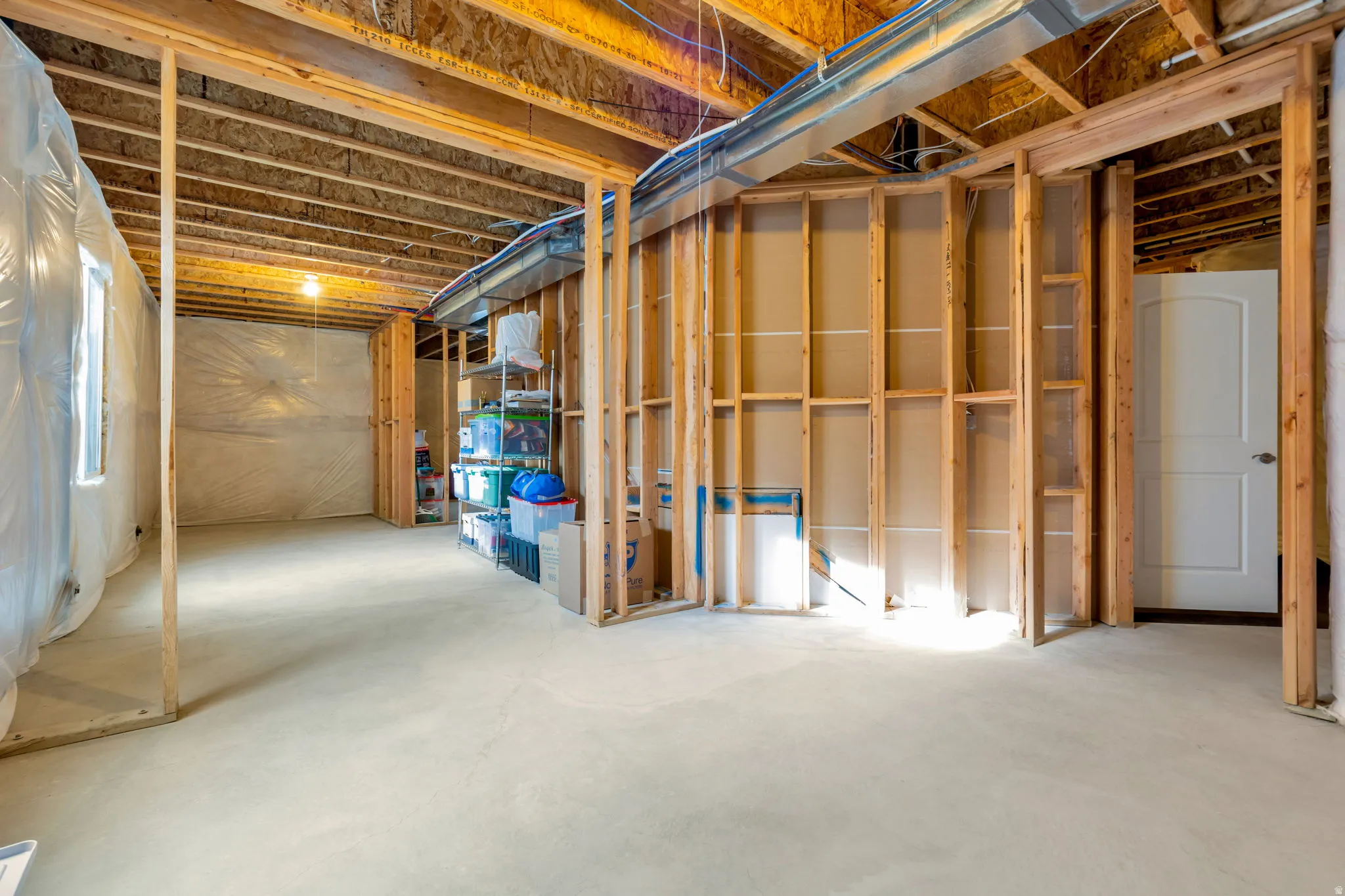 Unfinished basement with exposed wood framing, concrete flooring, visible ceiling joists, and a white interior door