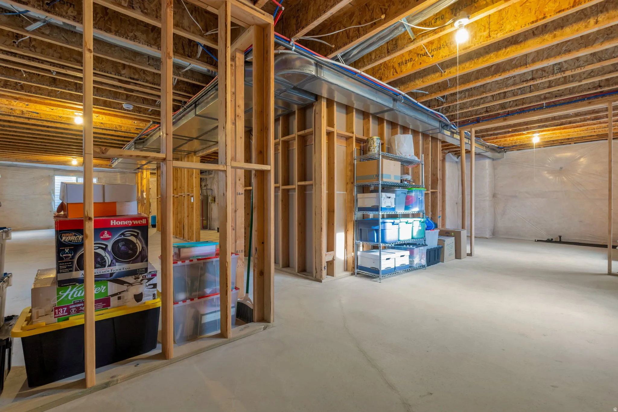 Unfinished basement featuring exposed wood framing, concrete flooring, overhead ductwork, and visible plumbing lines