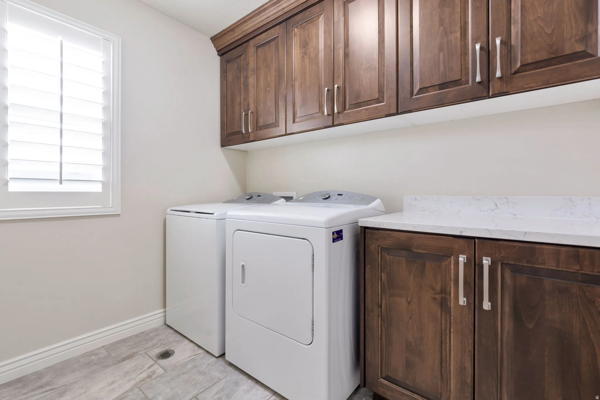 Dedicated laundry area featuring wood cabinetry with brushed nickel hardware, a white countertop, and plantation shutters