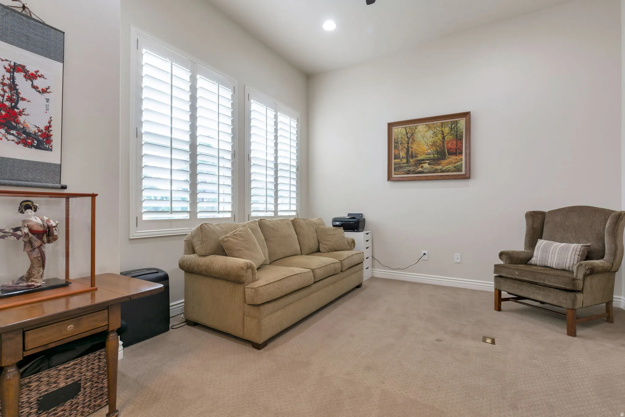 Spacious interior room featuring light-toned walls, neutral carpeting, and white window shutters
