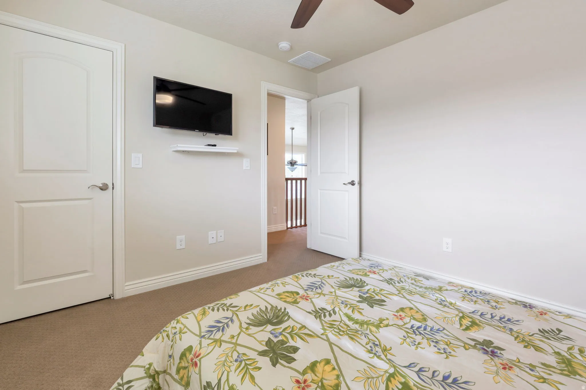 Carpeted interior room featuring a ceiling fan, a wall-mounted television, and a white interior door