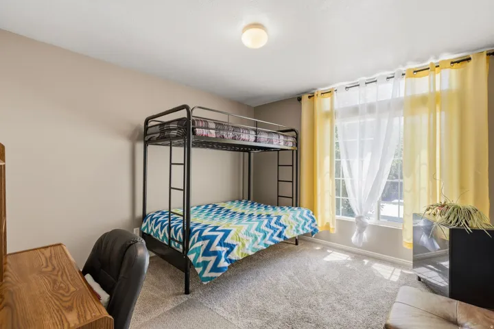 Bedroom with plush carpet flooring, neutral painted walls, and a large window featuring sheer and yellow drapes