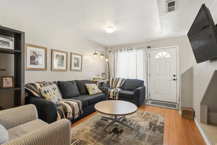 Living area featuring wood-finish flooring, a contemporary ceiling light fixture, a white entry door with an arched window, and a built-in shelving unit