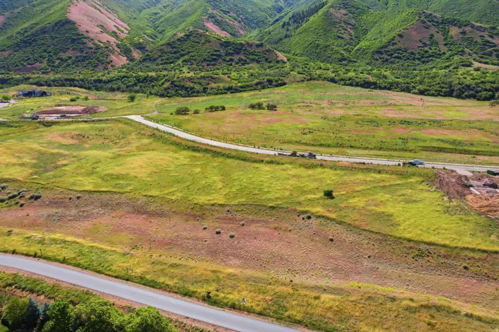 Expansive undeveloped land featuring a paved road, natural green and brown vegetation, and mountainous terrain in the background