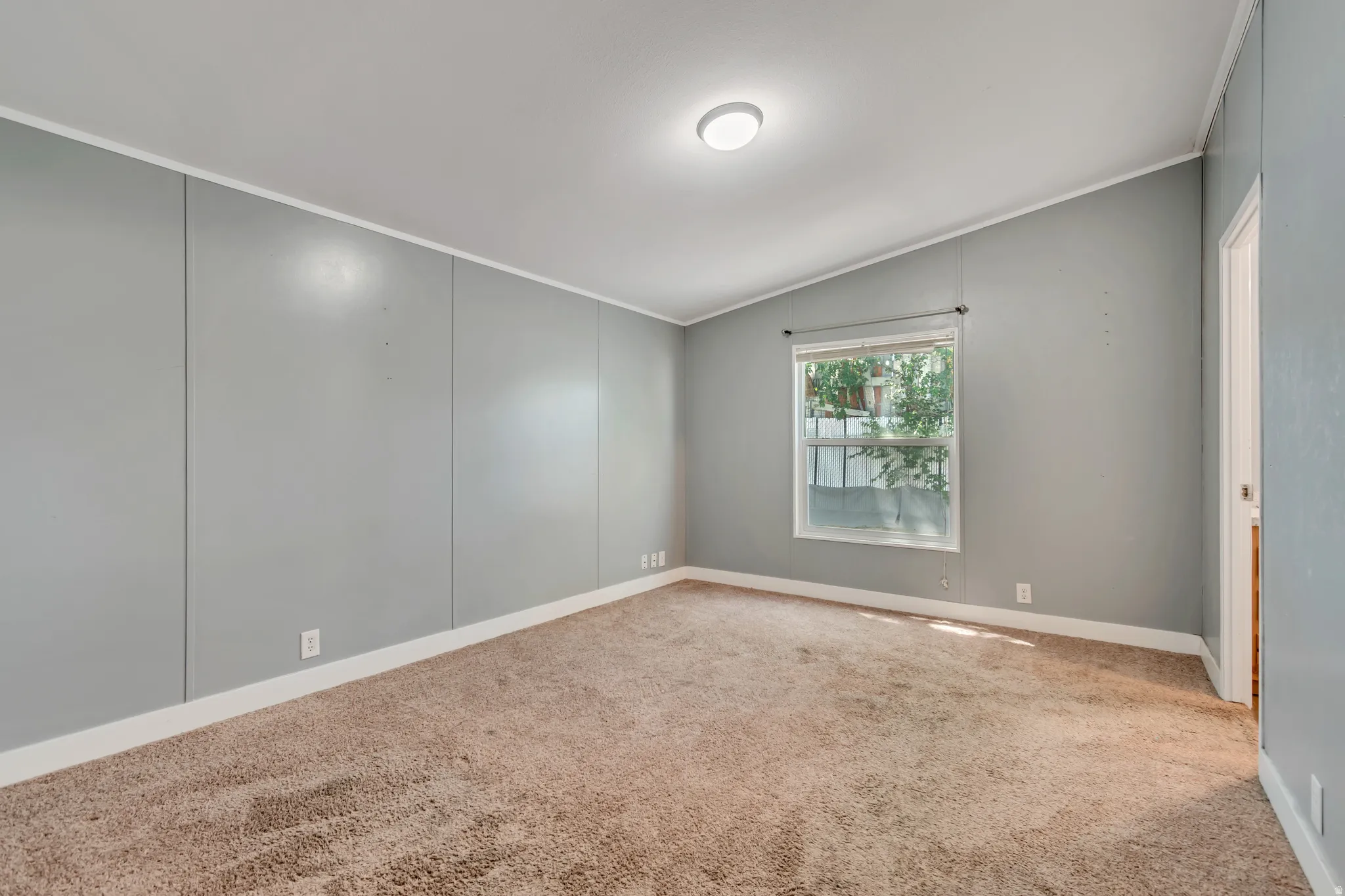 Interior room featuring a single window, vaulted ceiling, and neutral carpet flooring