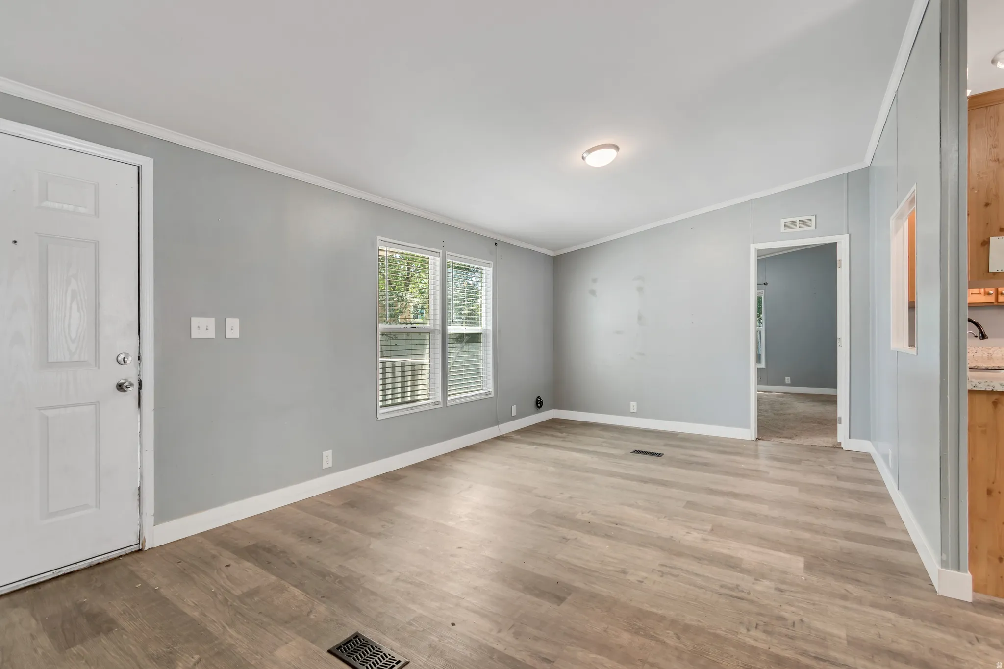 Open-concept living space featuring wood-finish flooring, light gray walls, white trim, and two windows with horizontal blinds