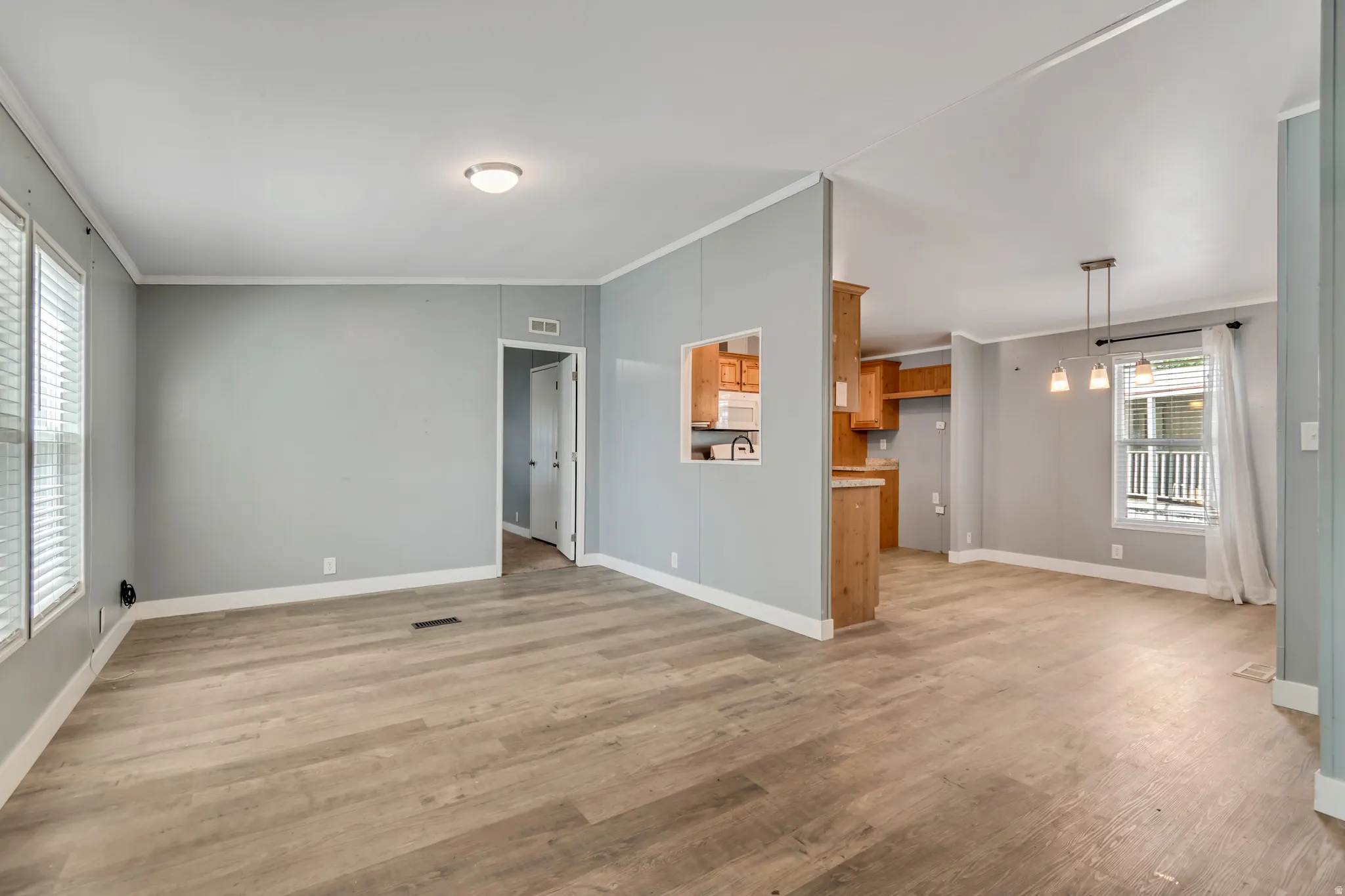 Spacious living area featuring light gray walls, wood-finish flooring, white baseboards, and a semi-flush mount ceiling light