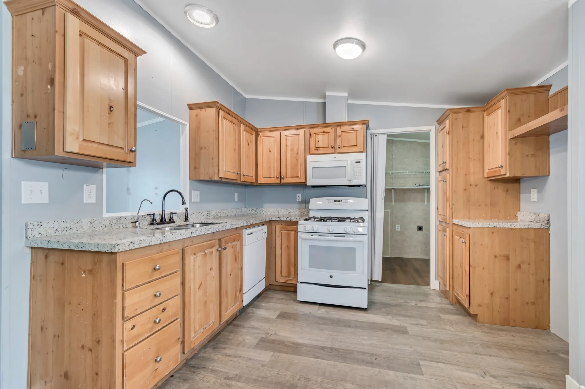 Kitchen featuring light wood cabinetry with silver-tone hardware, speckled countertops, a double basin sink with a matte black faucet, and white appliances including a gas range and microwave