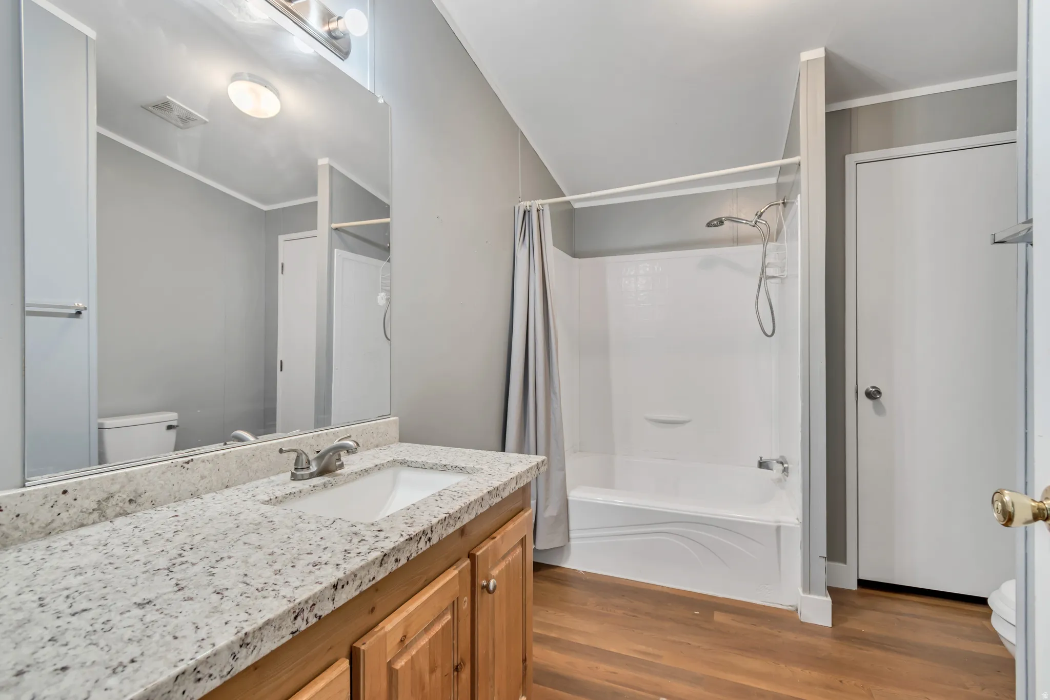 Bathroom featuring a wood-finish floor, light-toned vanity with a white countertop, and a shower-tub combination