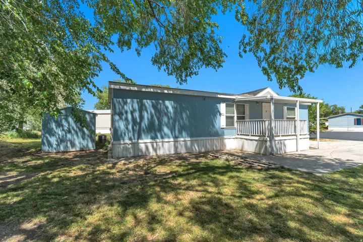 Blue manufactured home featuring a covered front porch with white railing, light-colored trim, and a separate blue utility shed