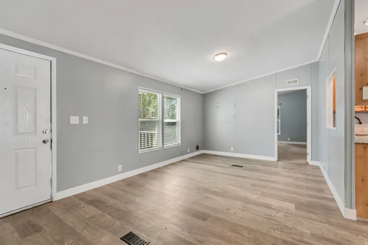 Open-concept living space featuring wood-finish flooring, light gray walls, white trim, and two windows with horizontal blinds