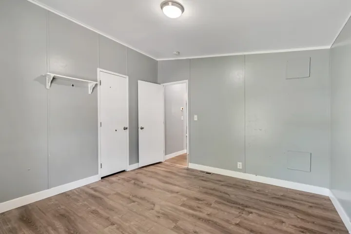 Interior space featuring wood-finish flooring, light gray wall paneling, white trim, a flush mount ceiling light, and multiple interior doors