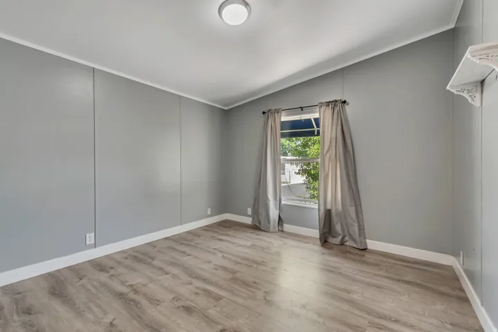 Spacious room featuring wood-finish flooring, light grey walls, white trim, and a window with a dark curtain rod
