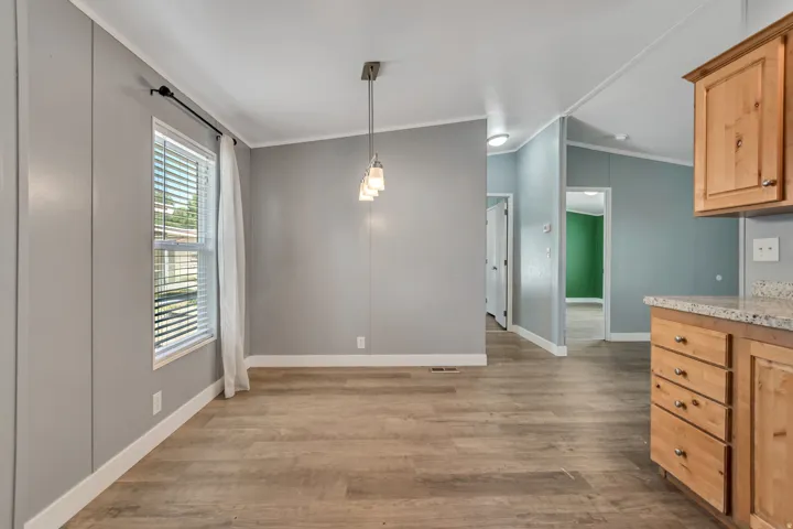 Open-concept dining area featuring wood-finish flooring, a contemporary pendant light fixture, and light gray panel walls
