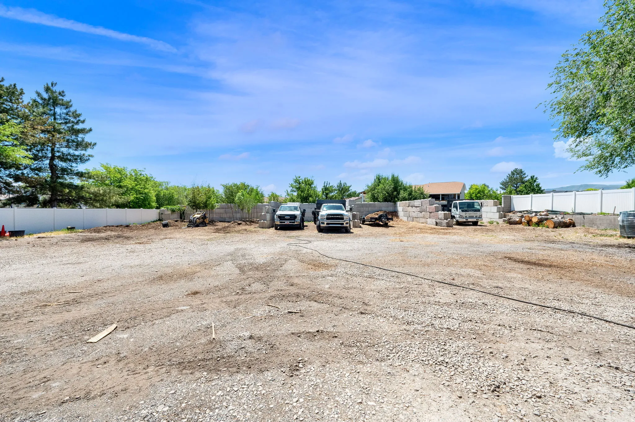 Expansive gravel lot featuring a white privacy fence and mature perimeter trees