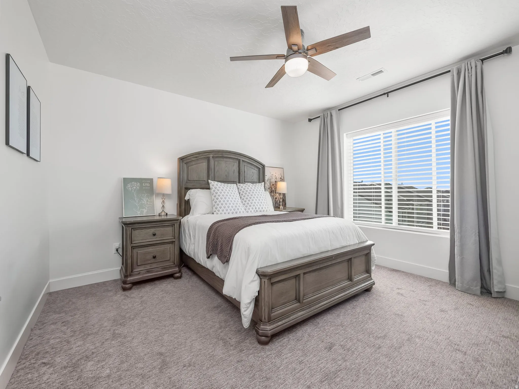 Spacious bedroom featuring neutral carpeting, a large window with horizontal blinds, and a ceiling fan with integrated lighting