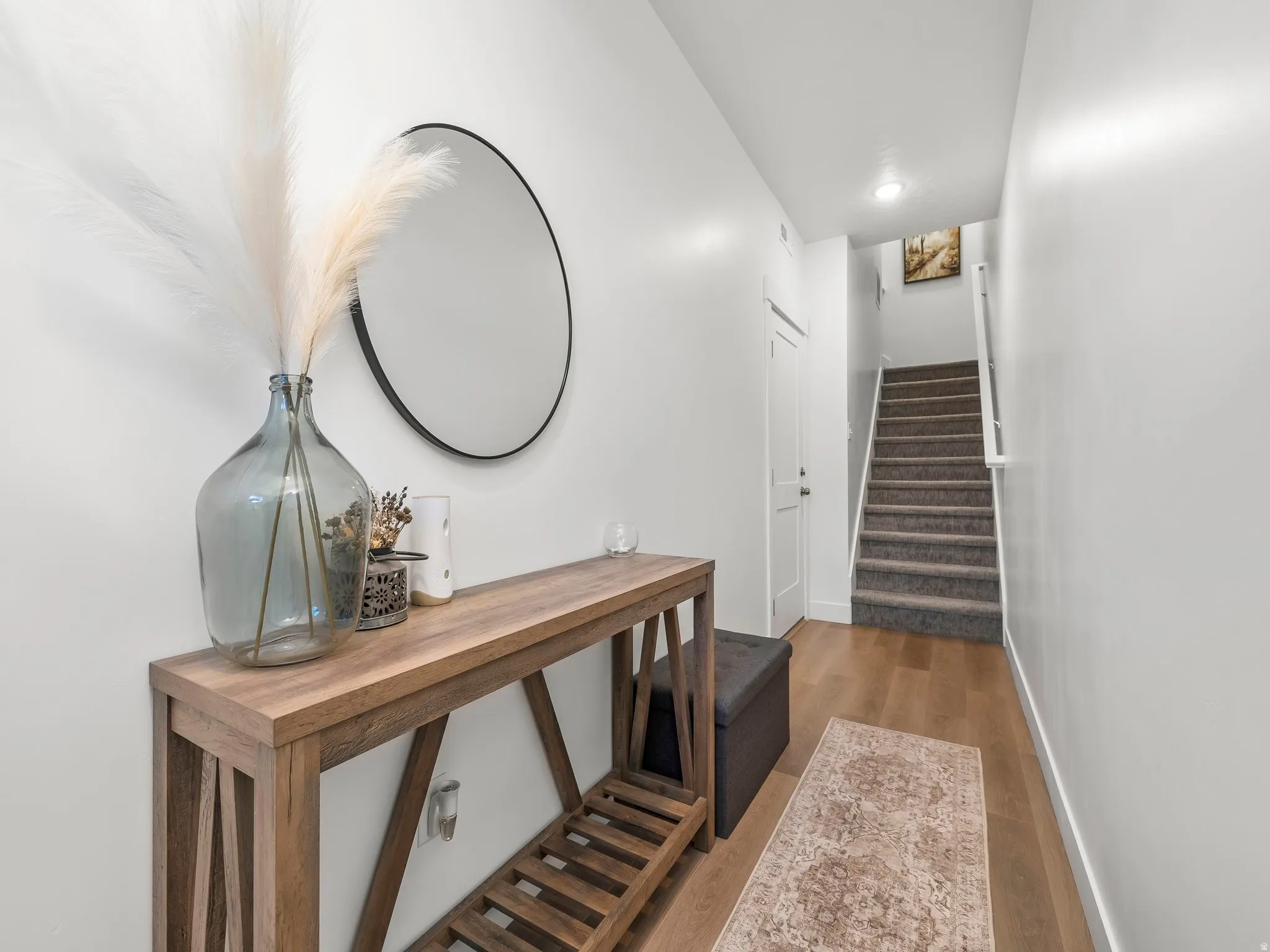 Entryway featuring wood-finish flooring, a contemporary accent wall mirror, and a staircase with carpeted treads