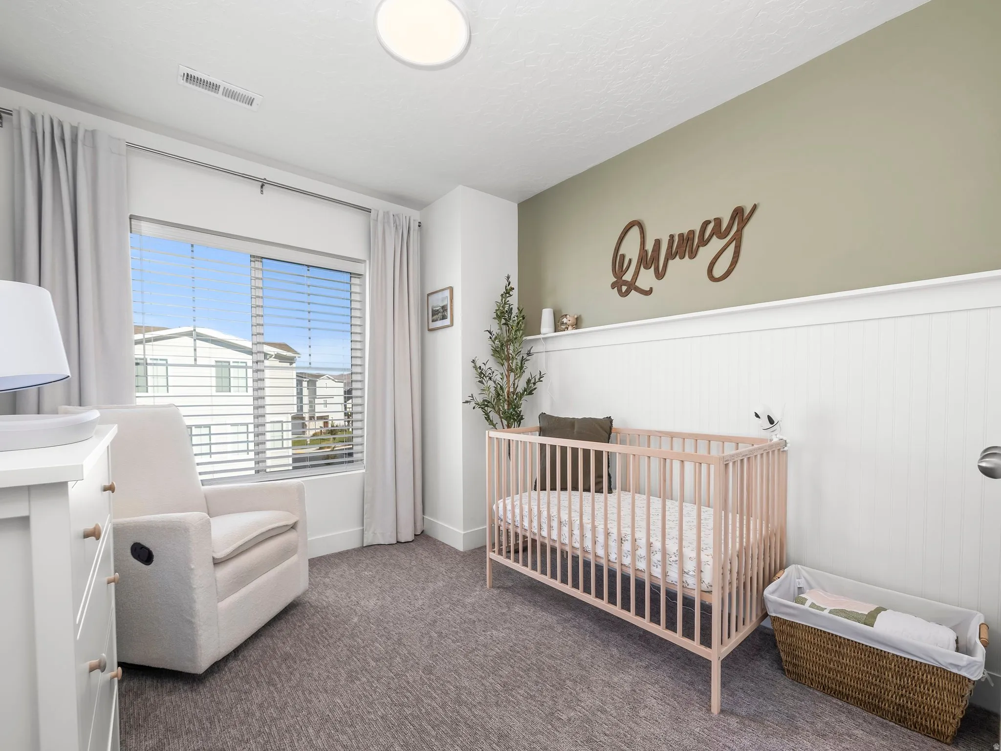 Room featuring a window with blinds and drapes, a two-tone wall with wainscoting, and textured carpet flooring