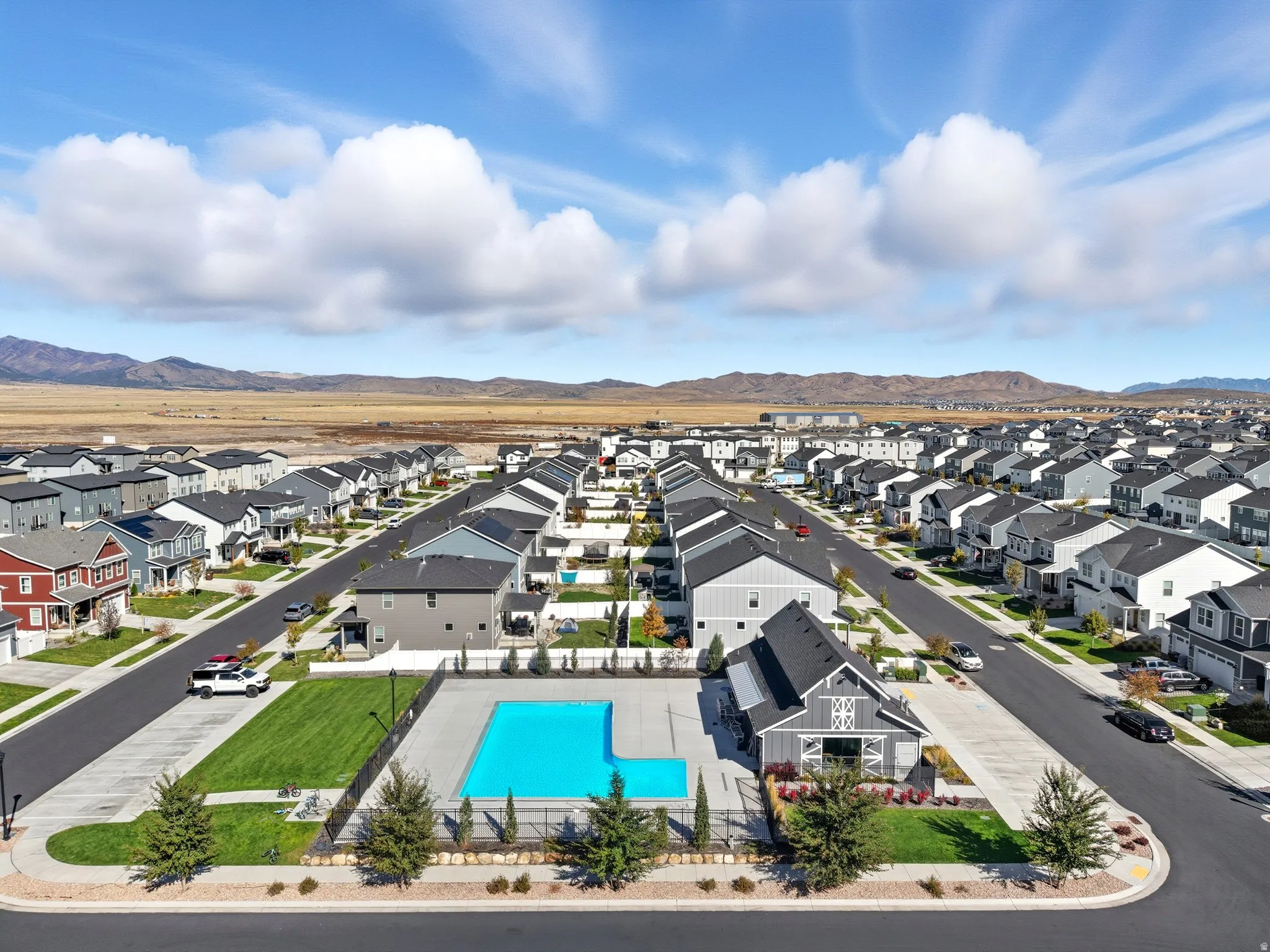 Aerial perspective showcasing a community with a central pool, clubhouse, and surrounding residential streets with homes, all set against a backdrop of distant mountains