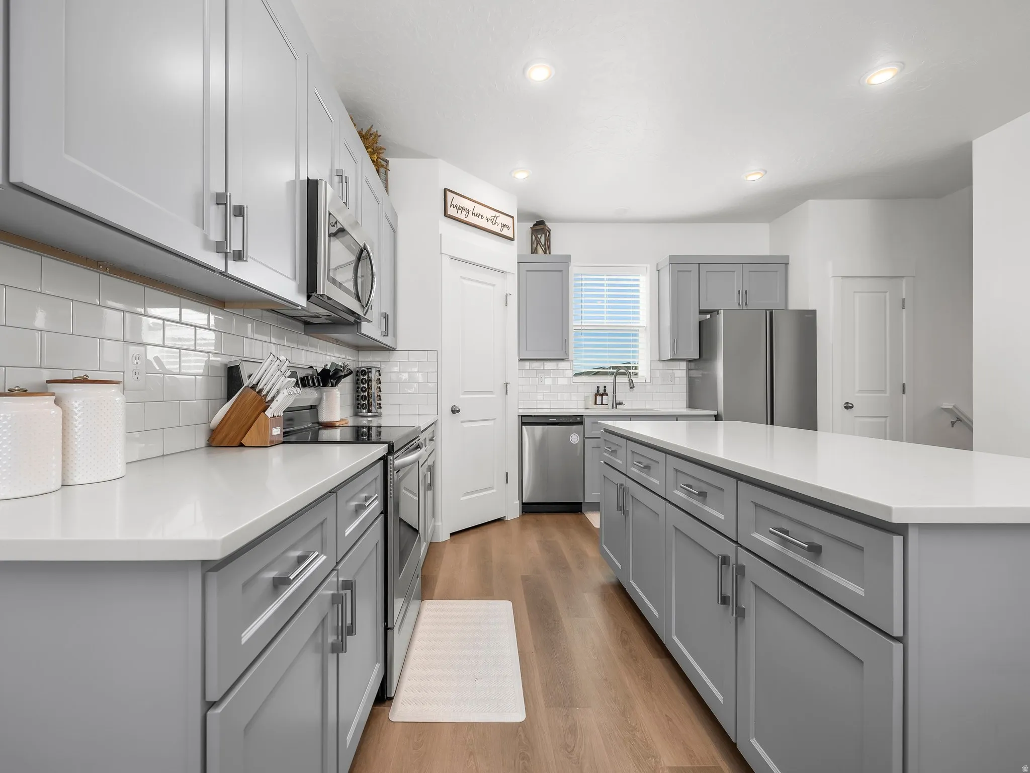 Kitchen featuring a spacious island, light gray shaker cabinetry, white subway tile backsplash, and light wood-finish flooring