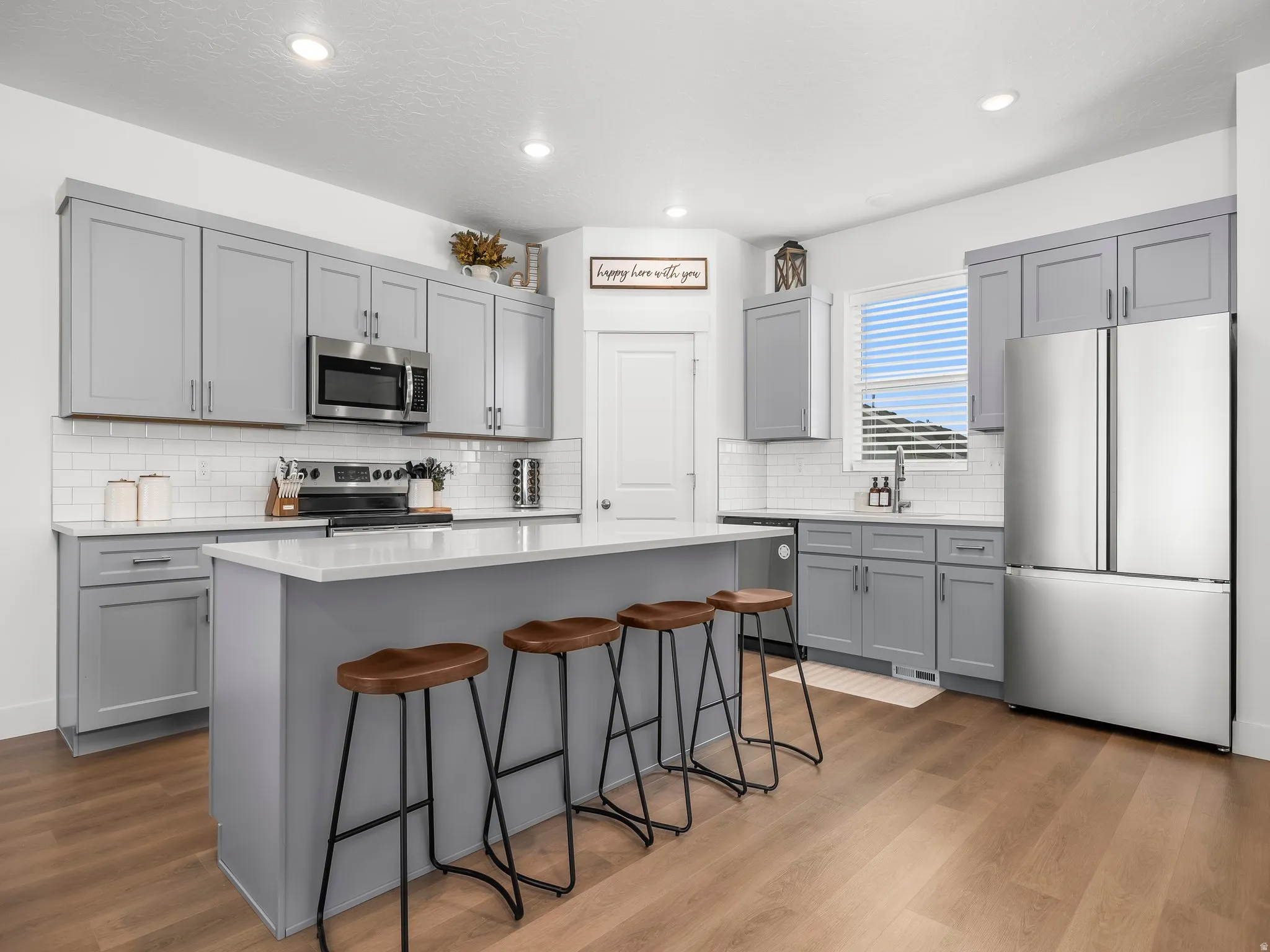 Contemporary kitchen featuring light gray cabinetry, stainless steel appliances, and wood-finish flooring