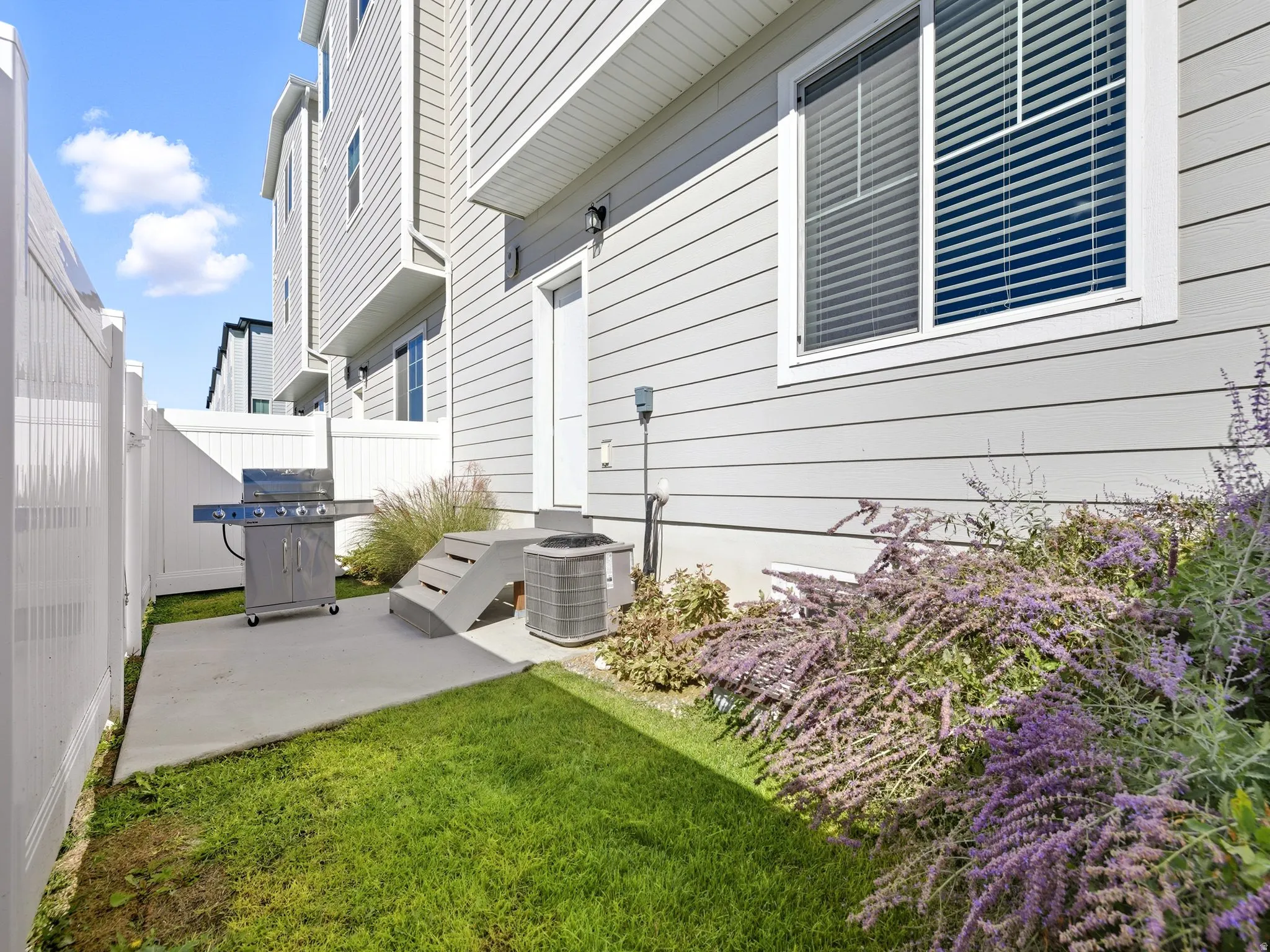 Fenced exterior patio featuring a concrete surface, green lawn, and flowering shrubs