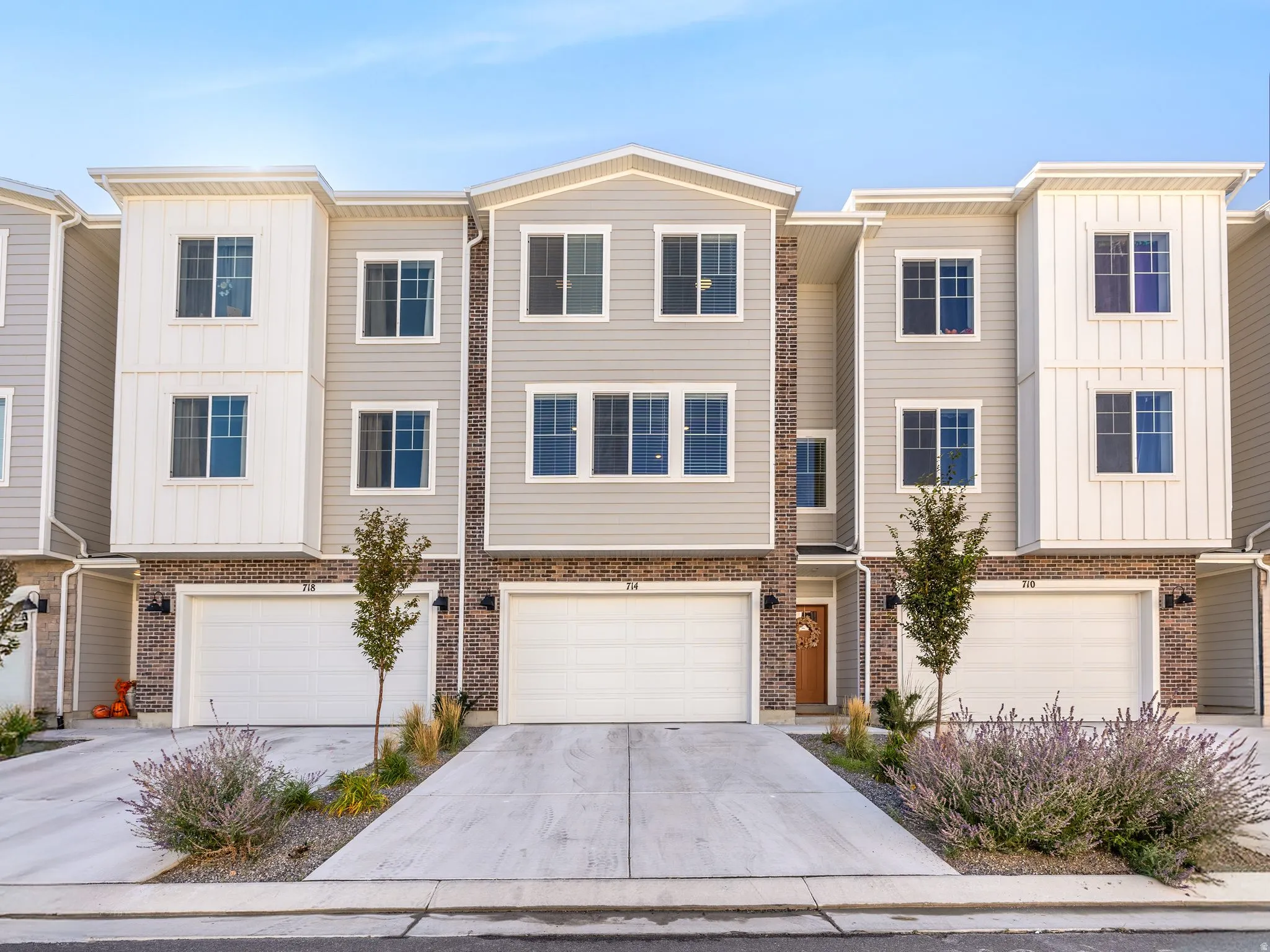 Modern townhome exterior featuring light gray siding, white vertical panel accents, brick veneer detailing, attached two-car garage, and a concrete driveway