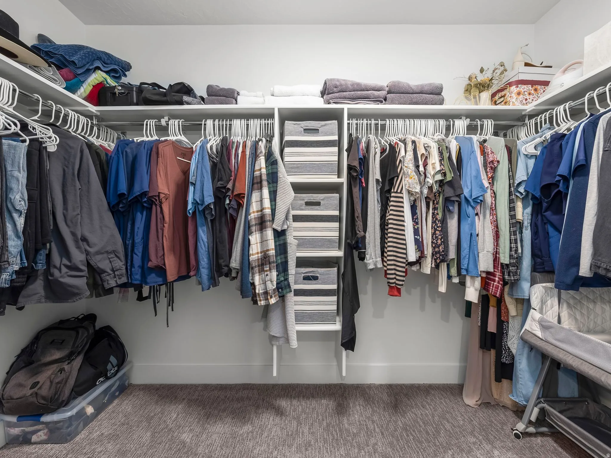Walk-in closet featuring built-in shelving, multiple hanging rods, corner shelving, and a neutral-toned carpet