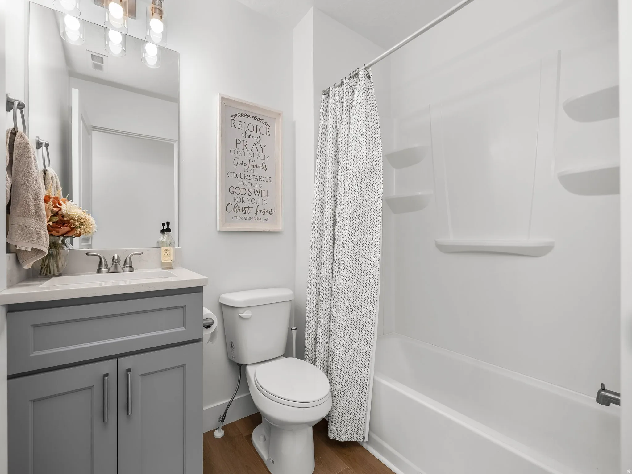 Bathroom featuring a spacious shower-tub combination with built-in shelving, a modern gray vanity with a light-toned countertop, and wood-finish flooring
