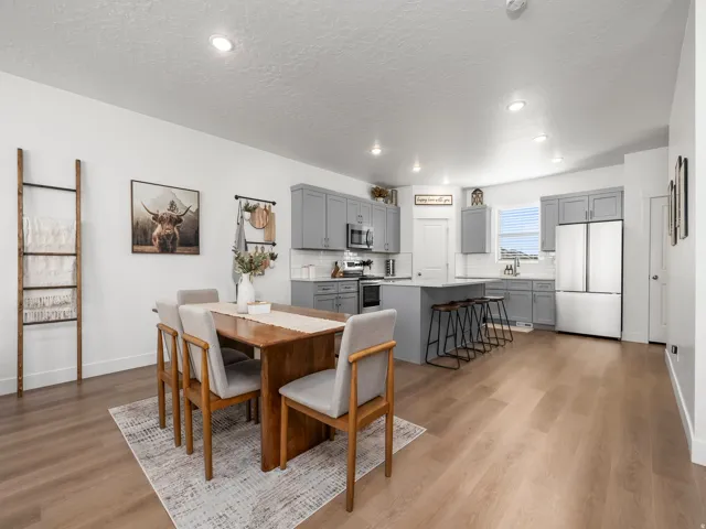 Open-concept dining and kitchen area featuring wood-finish flooring, recessed lighting, gray cabinetry, a kitchen island with seating, and stainless steel appliances