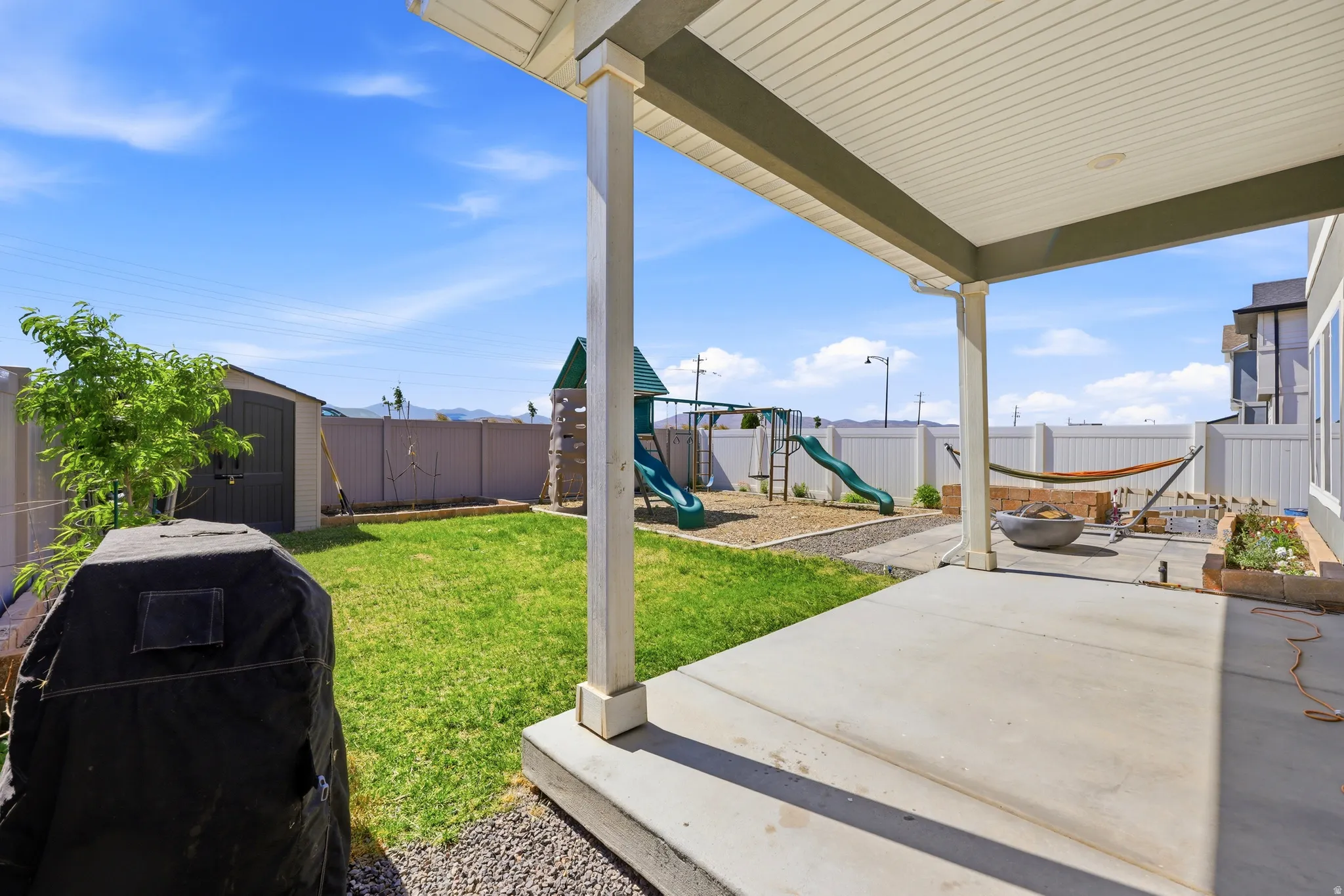 Covered concrete patio with white vinyl fencing and a gravel play area
