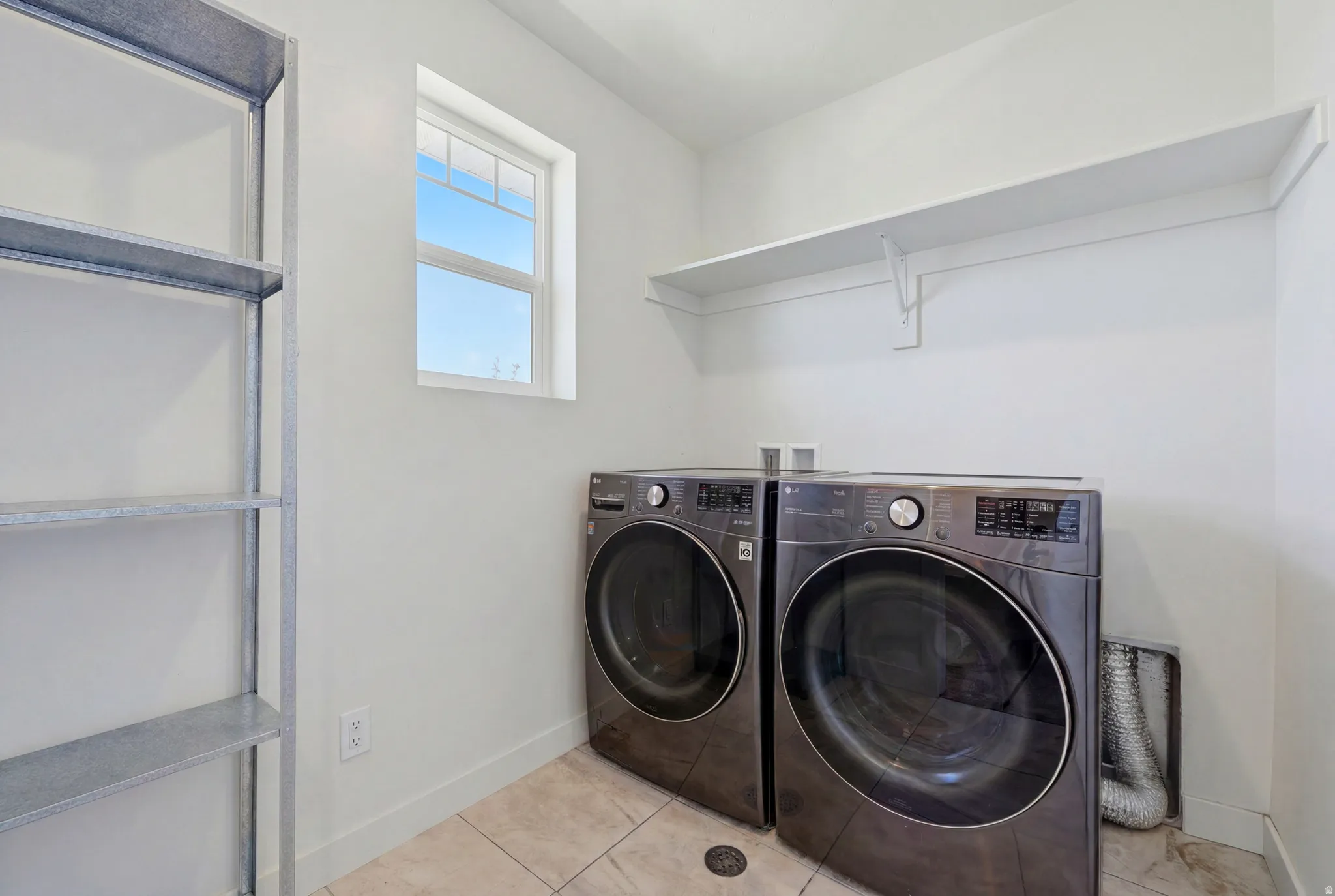 Laundry area featuring tile flooring, a window, wall-mounted shelving, and a freestanding metal shelving unit