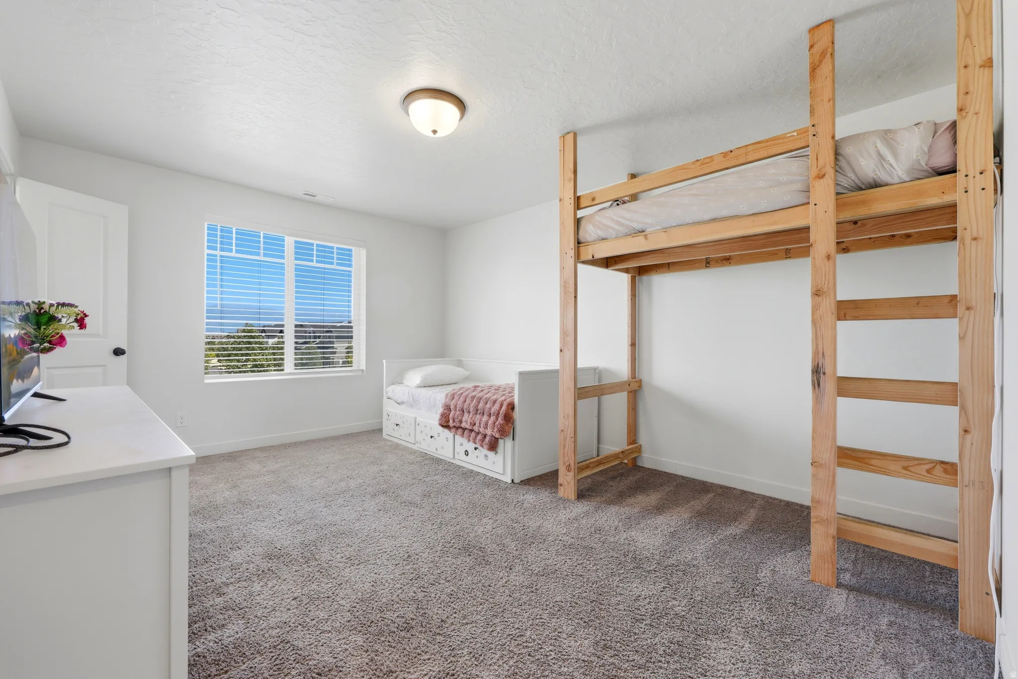 Bright room featuring a large window with blinds, neutral carpeting, and white walls