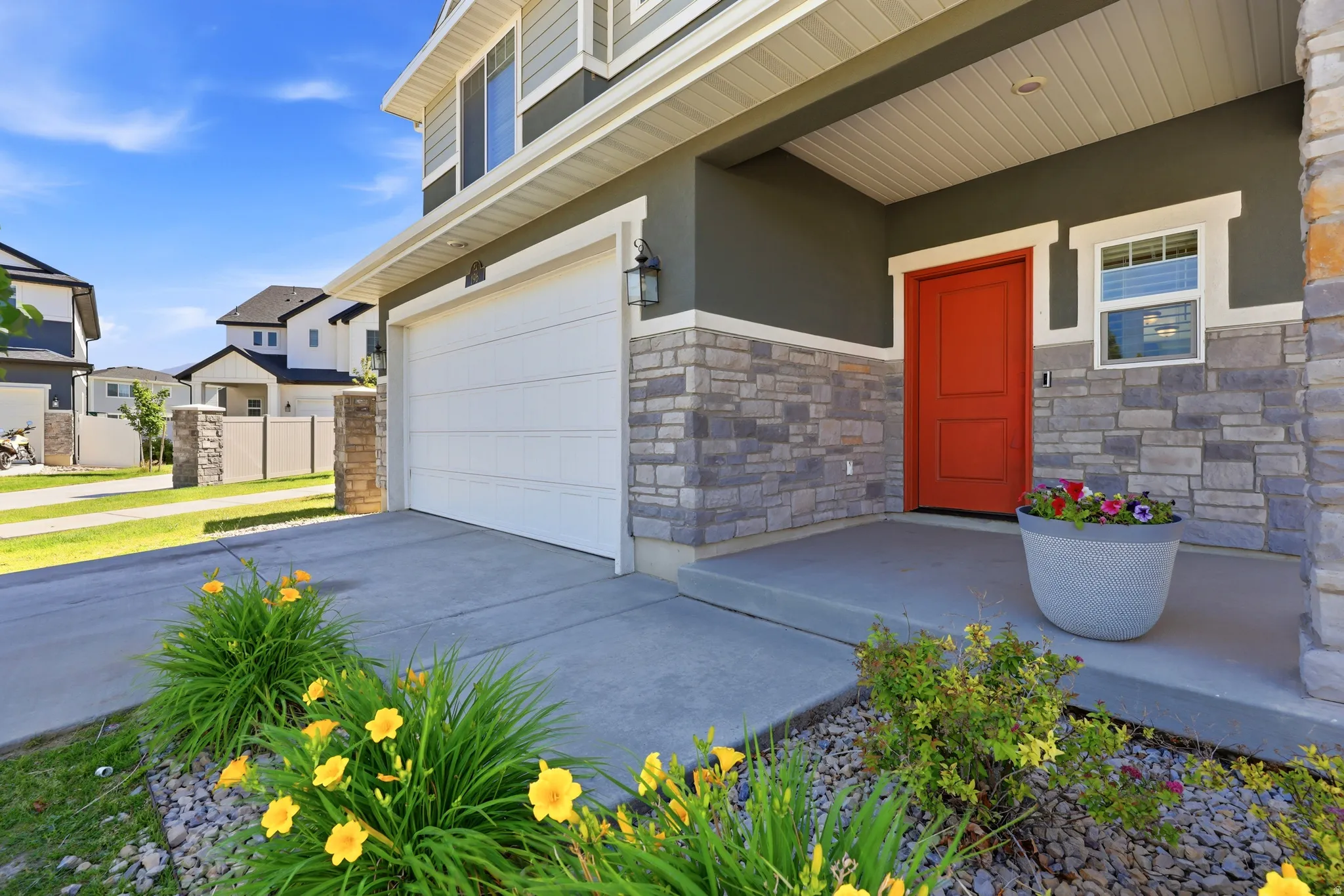 Exterior featuring a prominent red entry door, stacked stone veneer accents, and gray siding