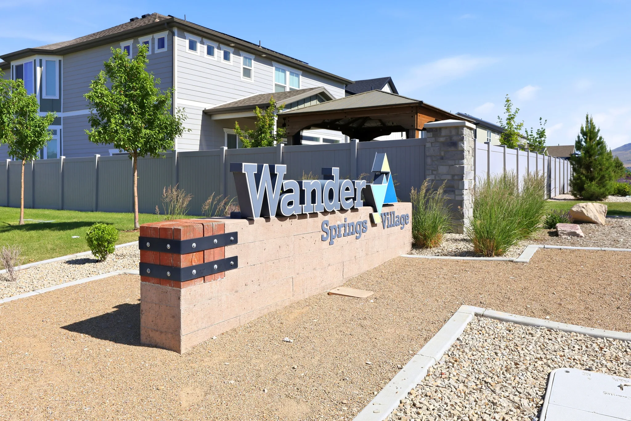 Stone-clad entry monument featuring dimensional lettering, textured block base, brick accents, and decorative metal strapping