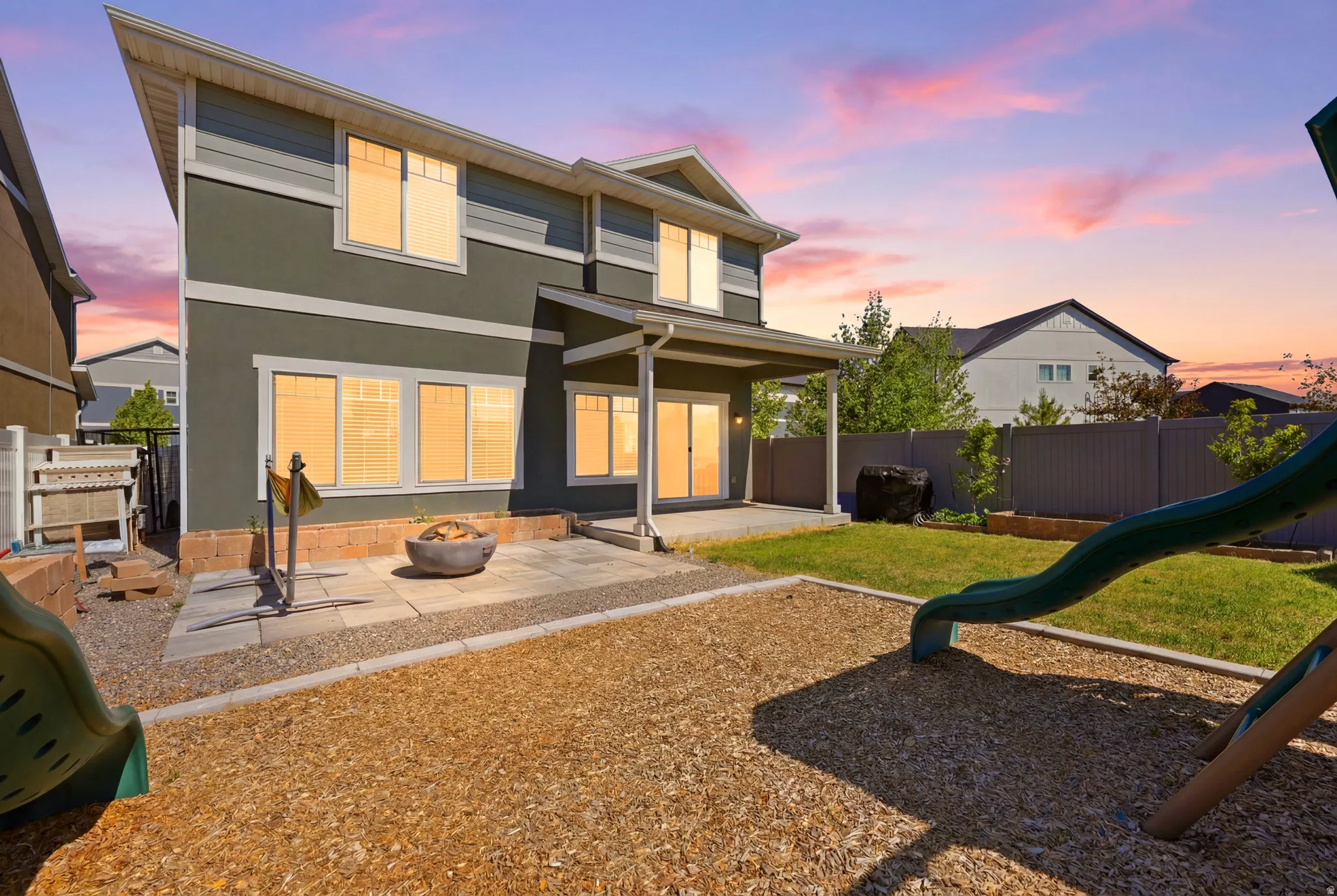 Spacious backyard featuring a covered patio, paved fire pit area, and a fenced perimeter