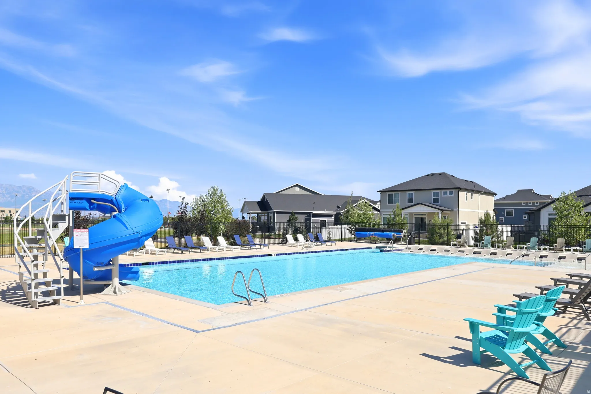 Community pool featuring an integrated water slide, surrounding lounge seating, and ample concrete decking