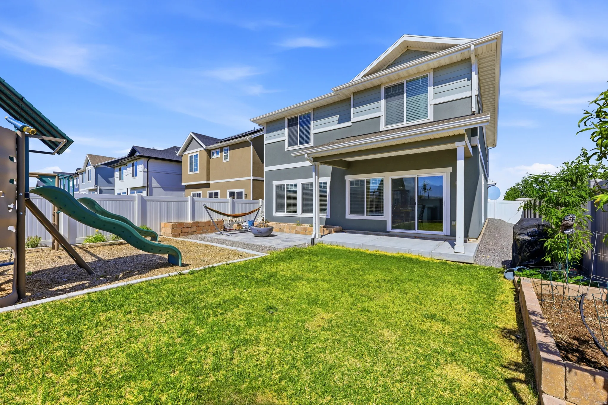 Expansive backyard featuring a green lawn, concrete patio, and a dedicated play area