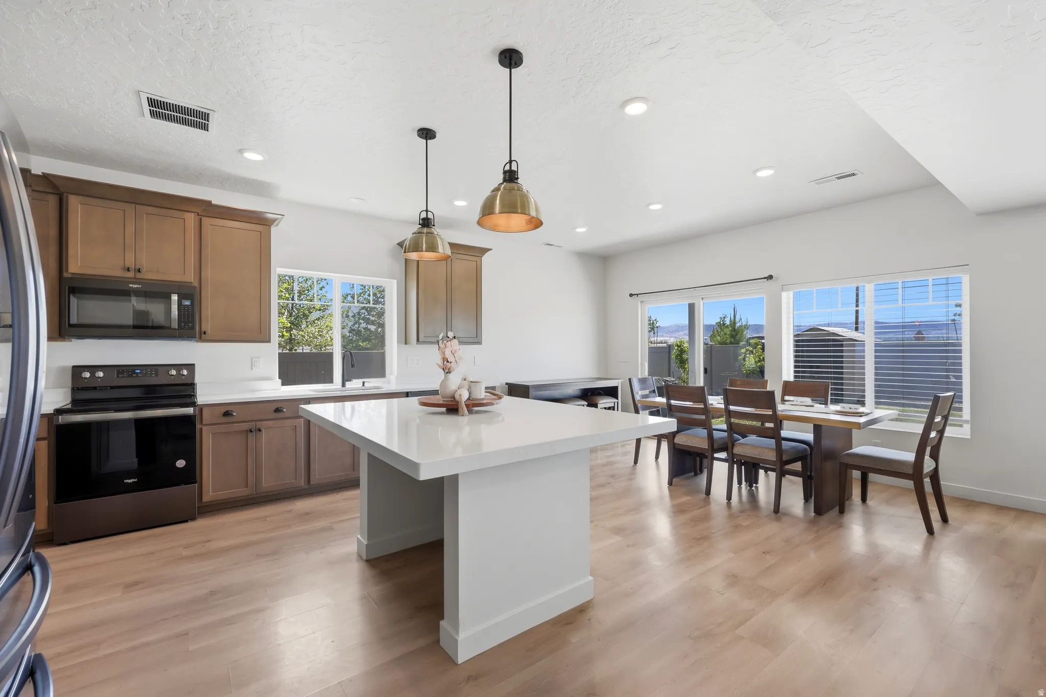 Open-concept kitchen and dining area featuring wood-finish flooring, a large island with a light-toned countertop, and recessed lighting